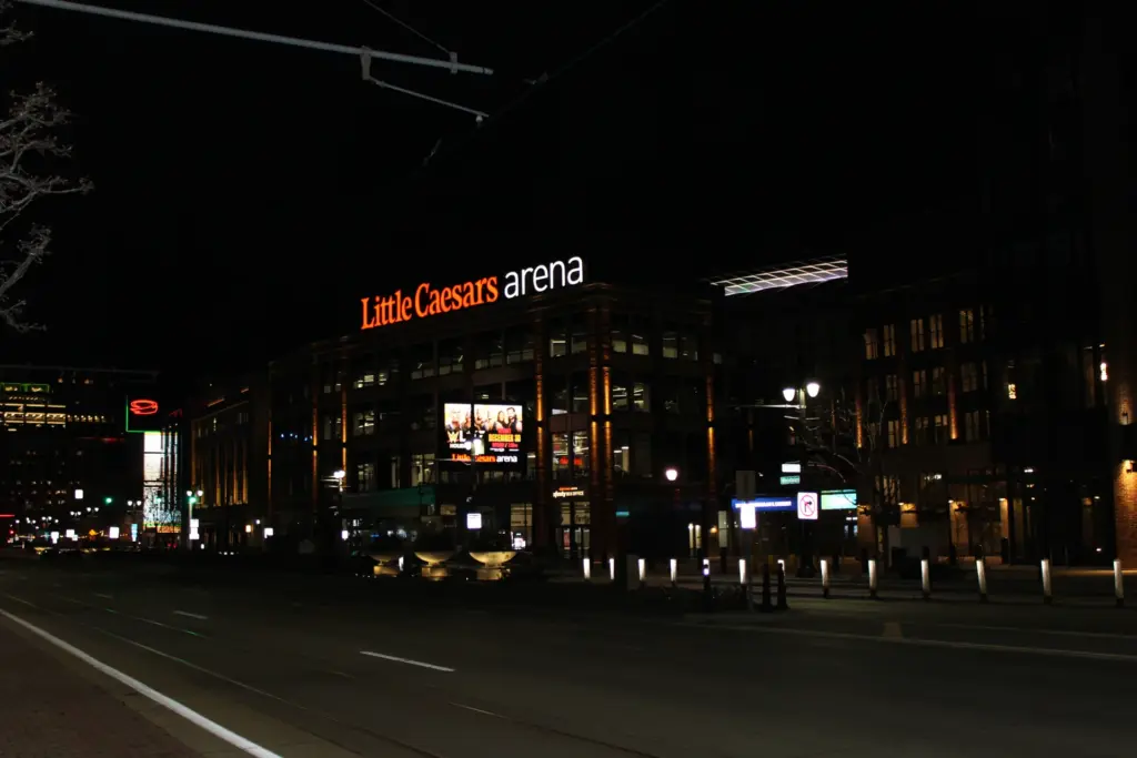 Осветеният вход на Little Caesars Arena през нощта.